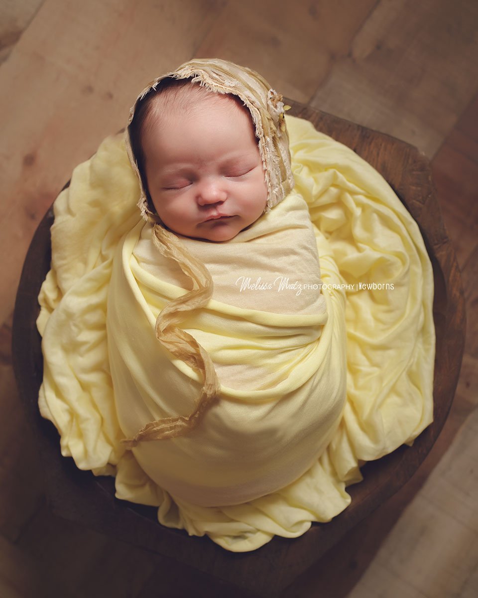 newborn-baby-girl-sleeping-in-a-bowl-yellow-bonnet-shelby-township-mi