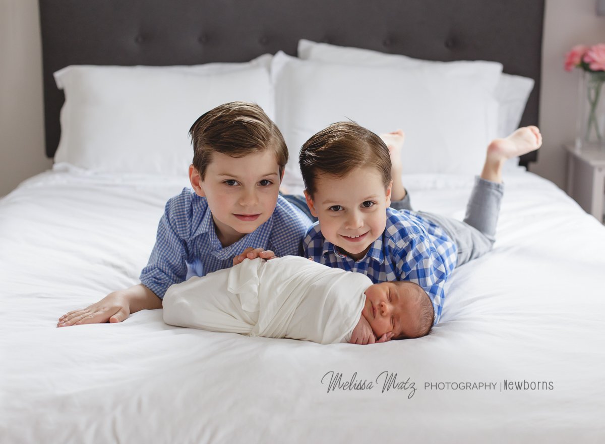 big brothers cuddled with newborn baby sister in home photo session