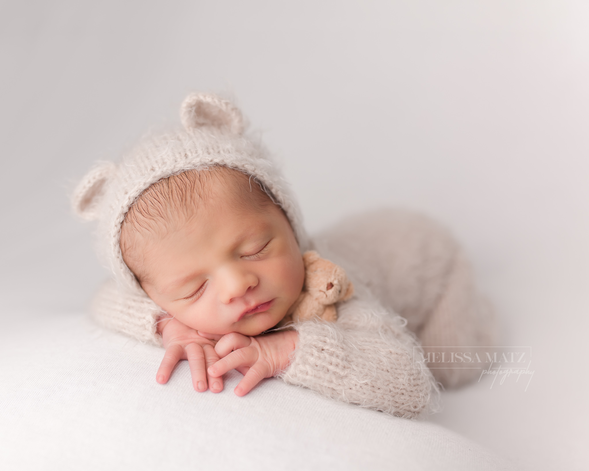 newborn baby boy in a bear bonnet and fuzzy romper sleeping with a tiny teddy bear in shelby township newborn photography studio