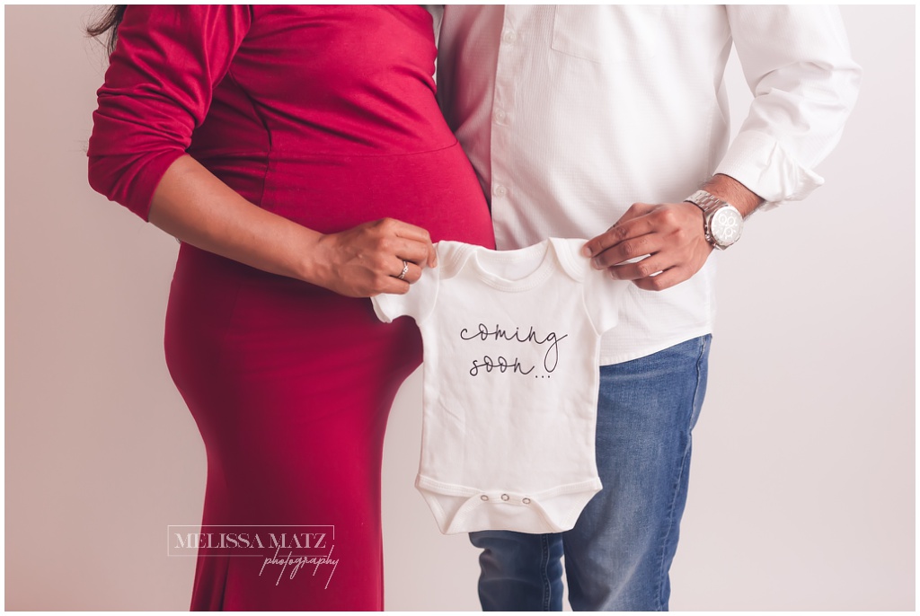 couple expecting a baby during their maternity session holding a coming soon onesie