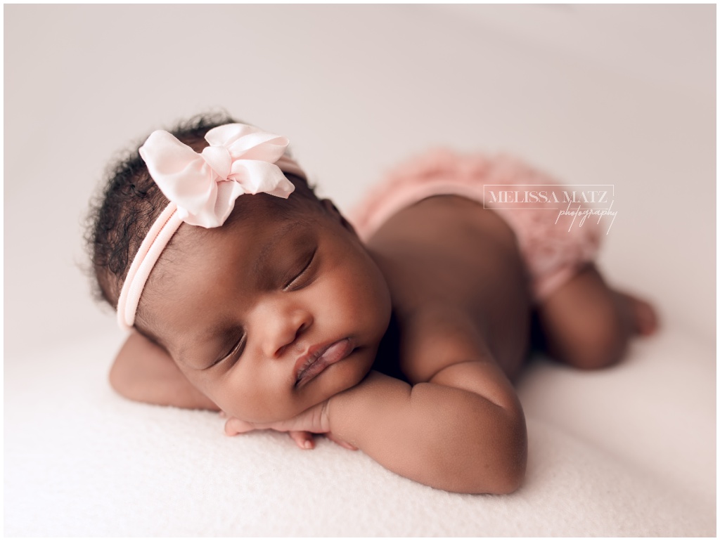 tiny newborn baby in pink romper during her newborn photography session held in macomb mi studio