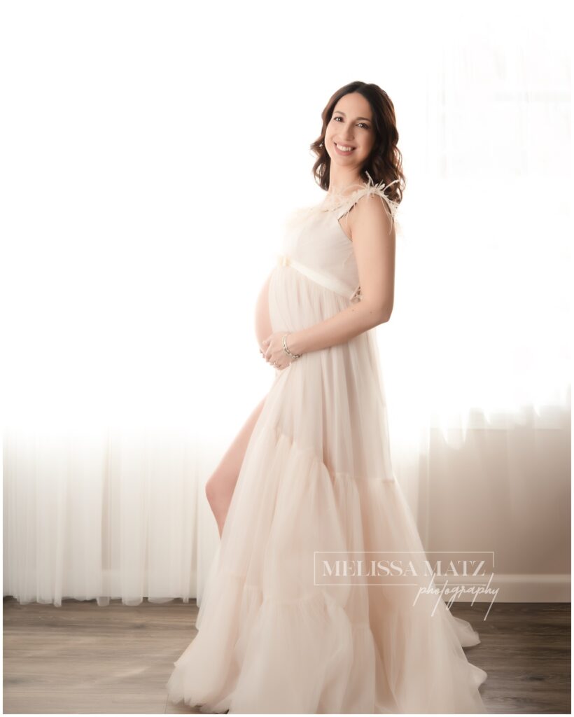 backlit maternity photo of mom to be in a cream tulle gown at her maternity photo session in metro detroit