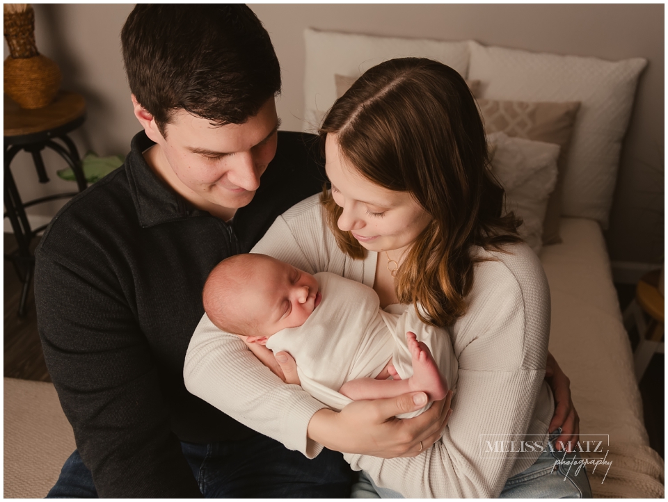 parents holding their newborn baby sitting in a newborn photography studio in metro detroit