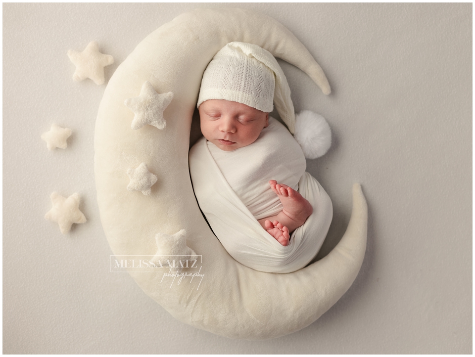 newborn wrapped in white on a white moon during his newborn photography session