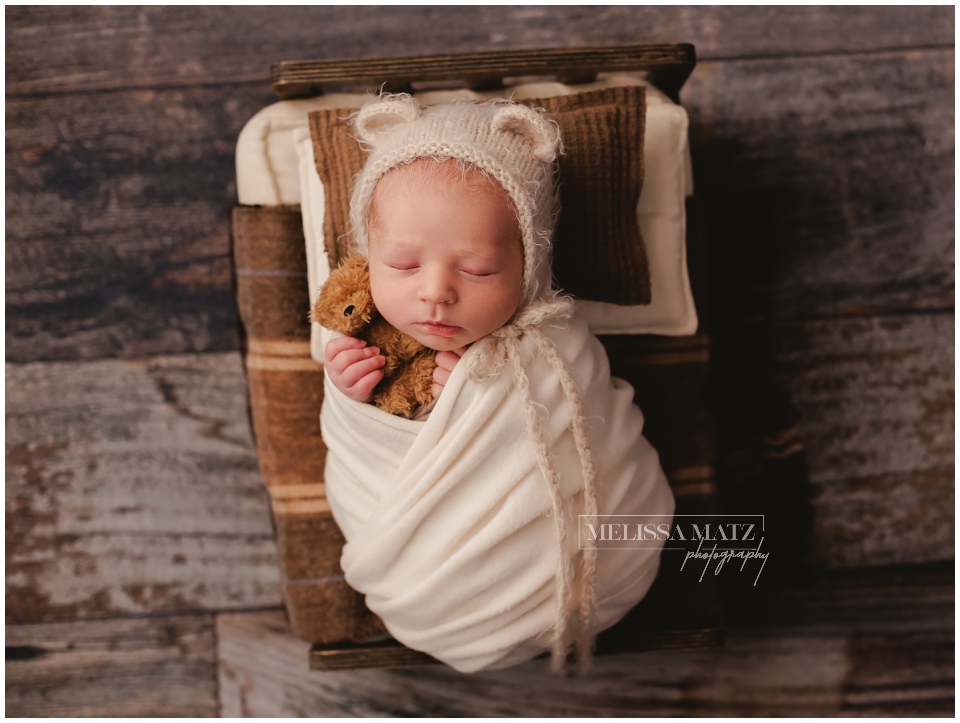swaddle wrapped newborn baby holding a tiny teddy bear during his newborn photo session