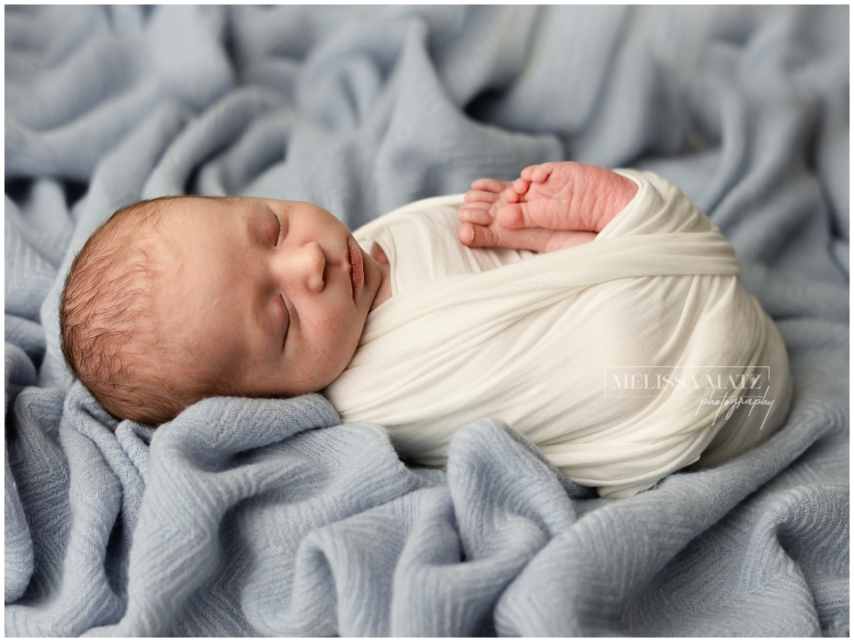baby wrapped in white sleeping on blue blanket