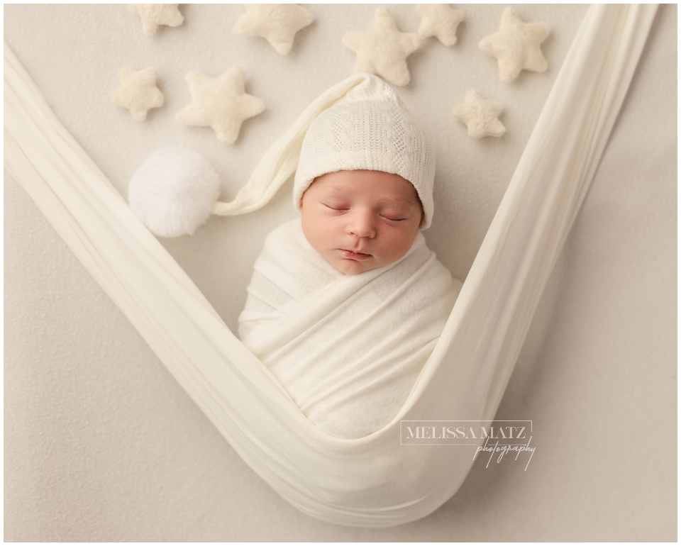 newborn wrapped in white with a bonnet surrounded by stars