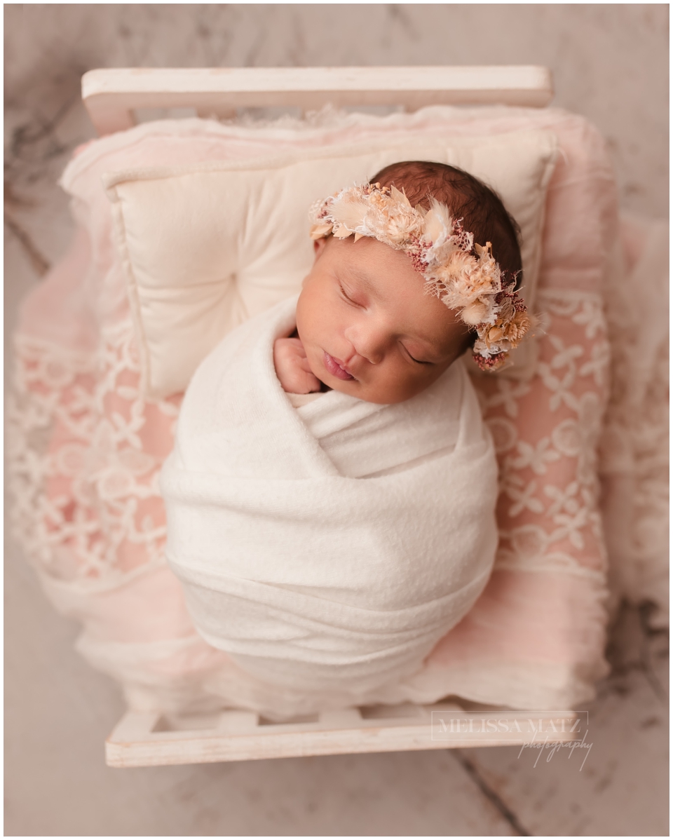 Newborn baby girl sleeping peacefully wearing a delicate floral headband, photographed in Shelby Township studio