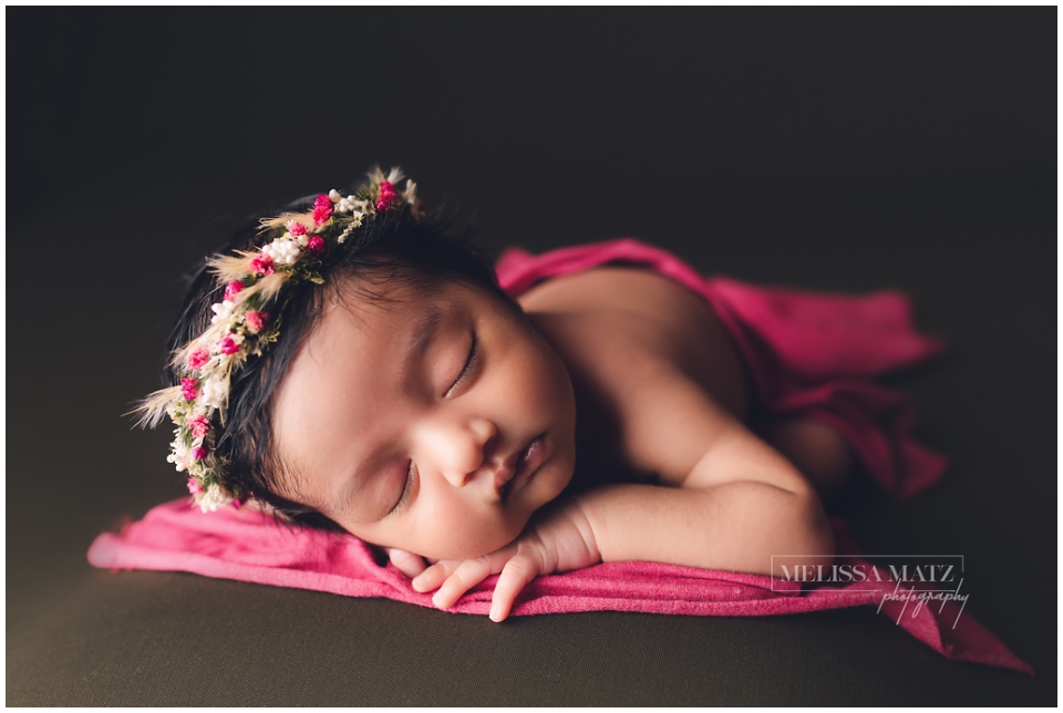 Newborn baby girl sleeping peacefully wearing a delicate floral headband, photographed in Utica Mi studio.