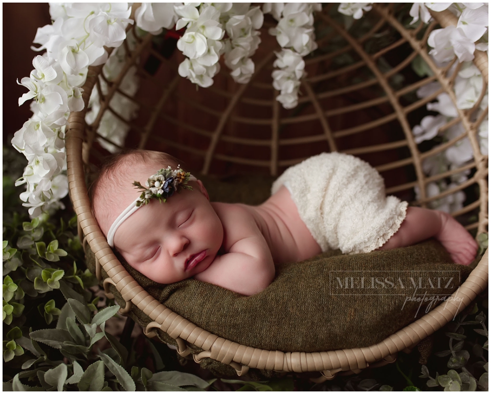 Floral-themed newborn portrait session with baby sleeping surrounded by plants and white flowers