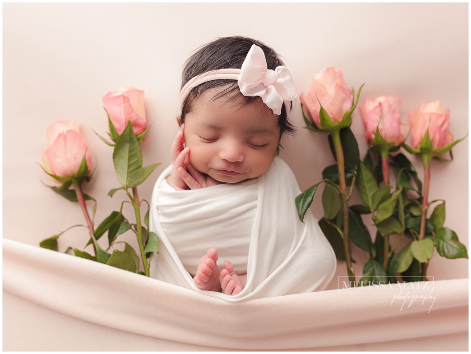 Shelby Township studio newborn photo with baby wrapped in neutral tones and framed by garden-inspired flowers.