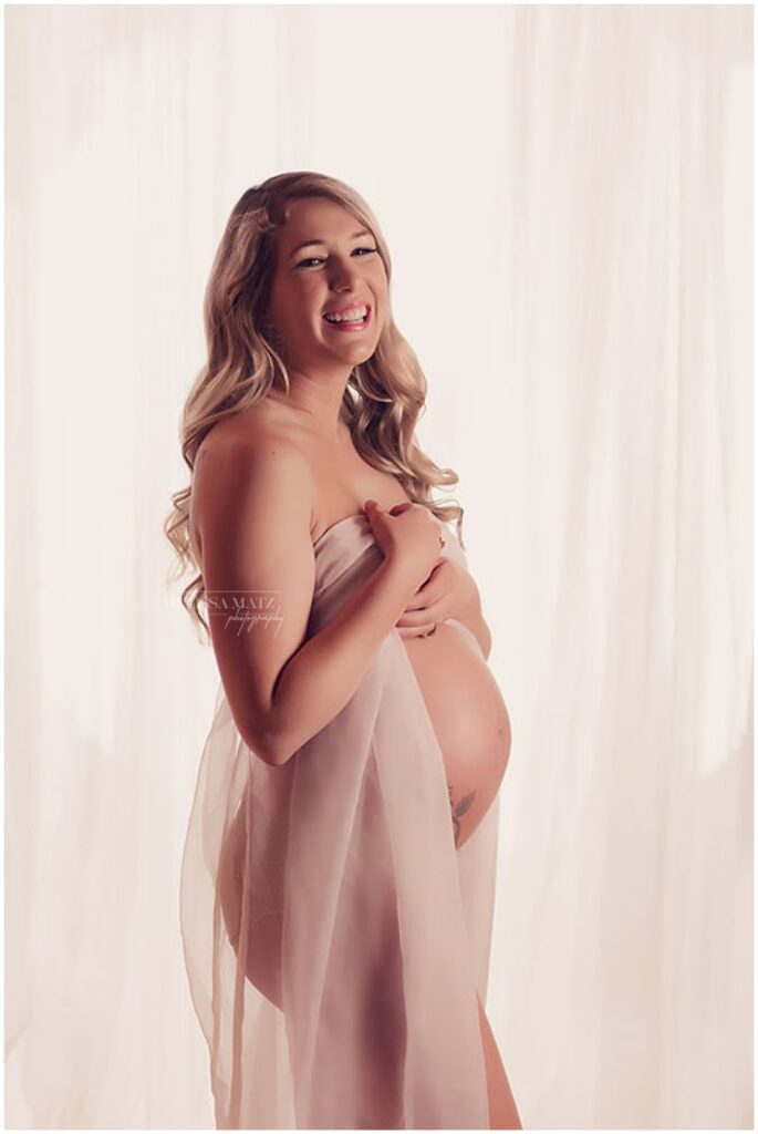 Soft-focus maternity boudoir photo with sheer fabric and natural light