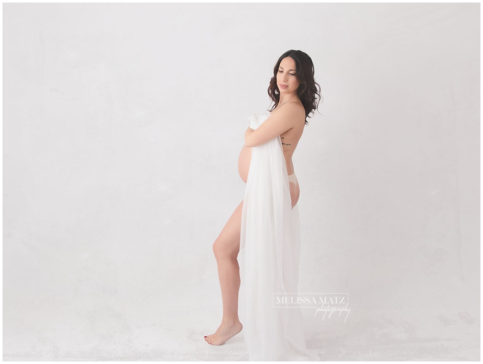 Confident mom-to-be draped in sheer fabric during intimate maternity photo session with Metro Detroit boudoir photographer