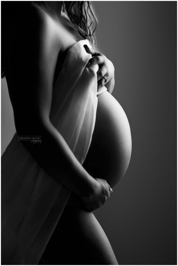 Black and white maternity boudoir image showcasing baby bump and glowing skin