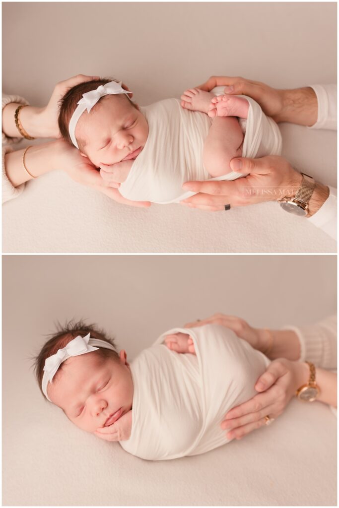 Parents cradling their newborn baby swaddle wrapped in white, with a cream backdrop.