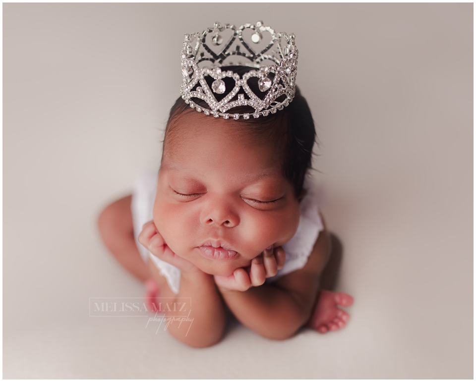 tiny newborn baby with her hands under her chin wearing a silver crown