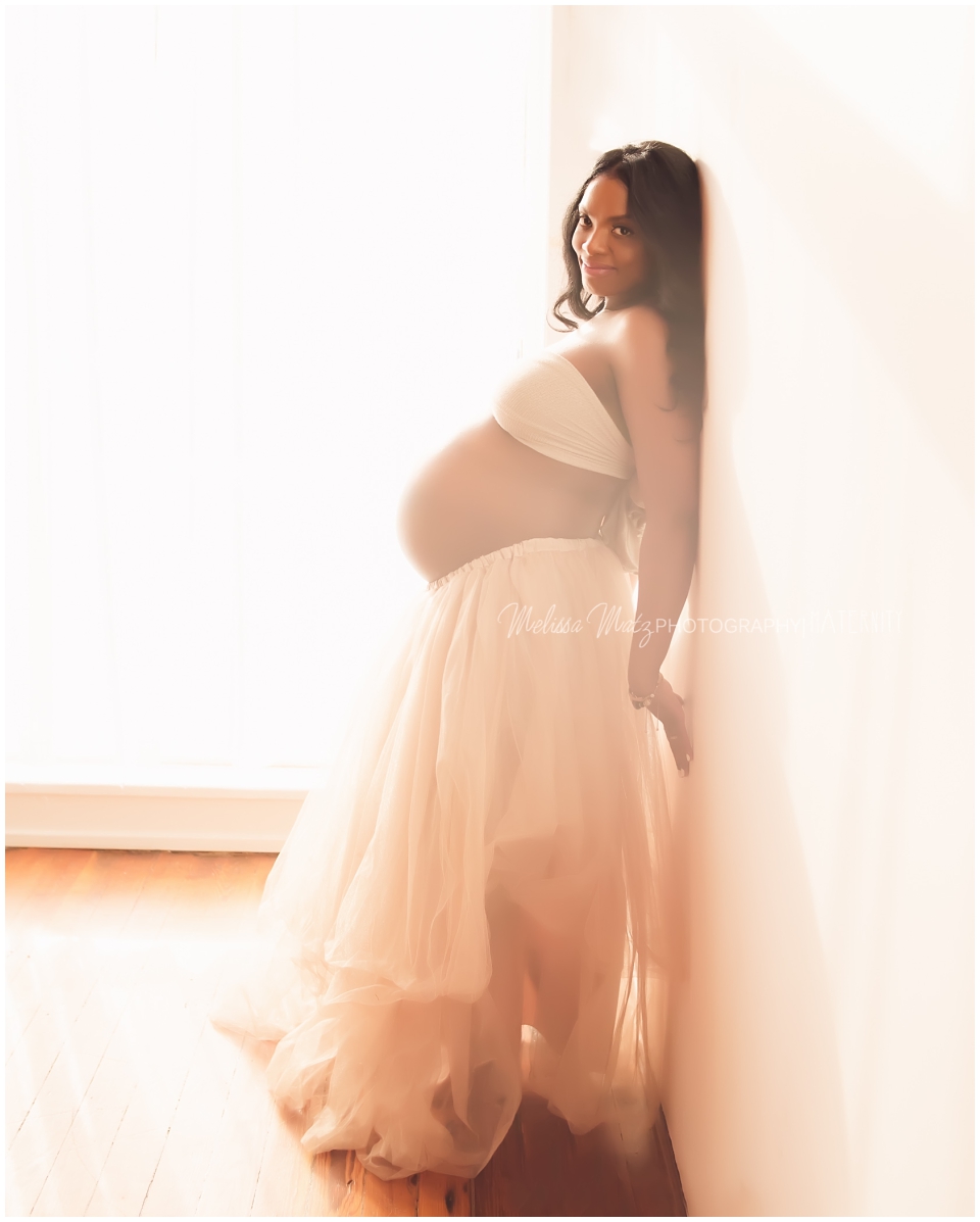 maternity photo session in studio against a window mom in gold tulle skirt