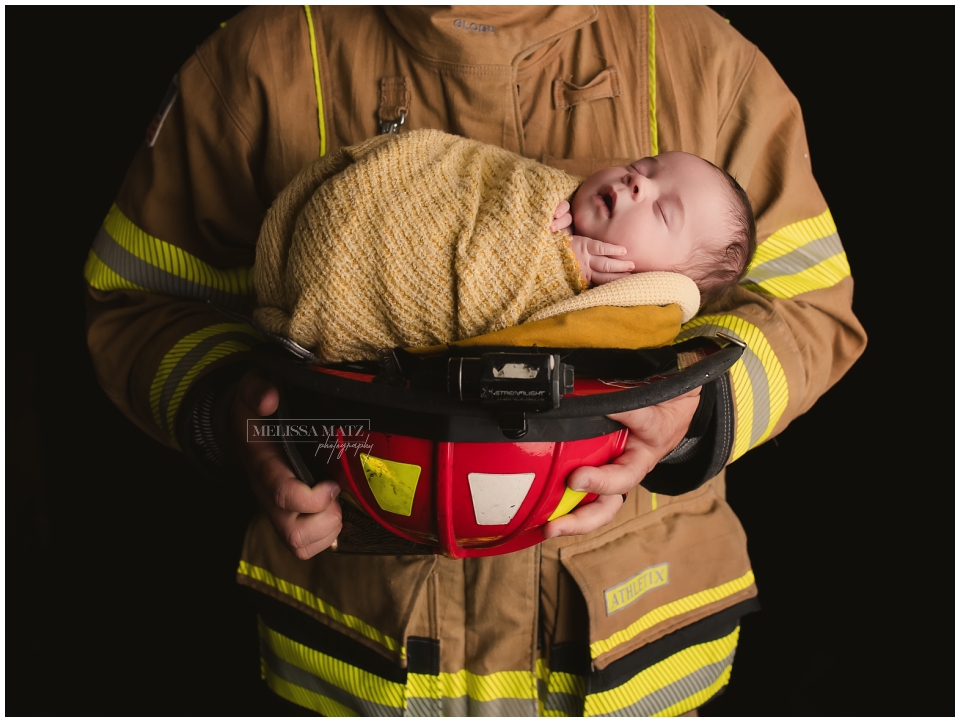 Newborn nestled in firefighter helmet as dad wears fire coat father’s taken in Metro Detroit newborn session photo