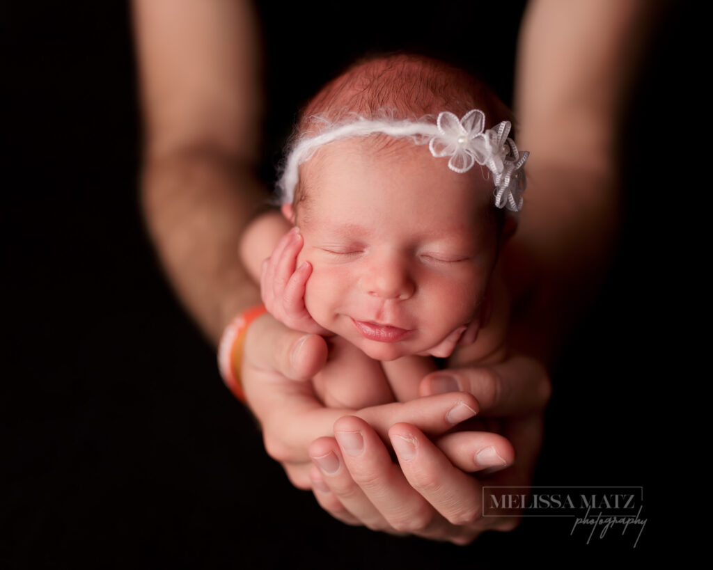 tiny newborn baby with her hands on her cheeks held in dad's hands