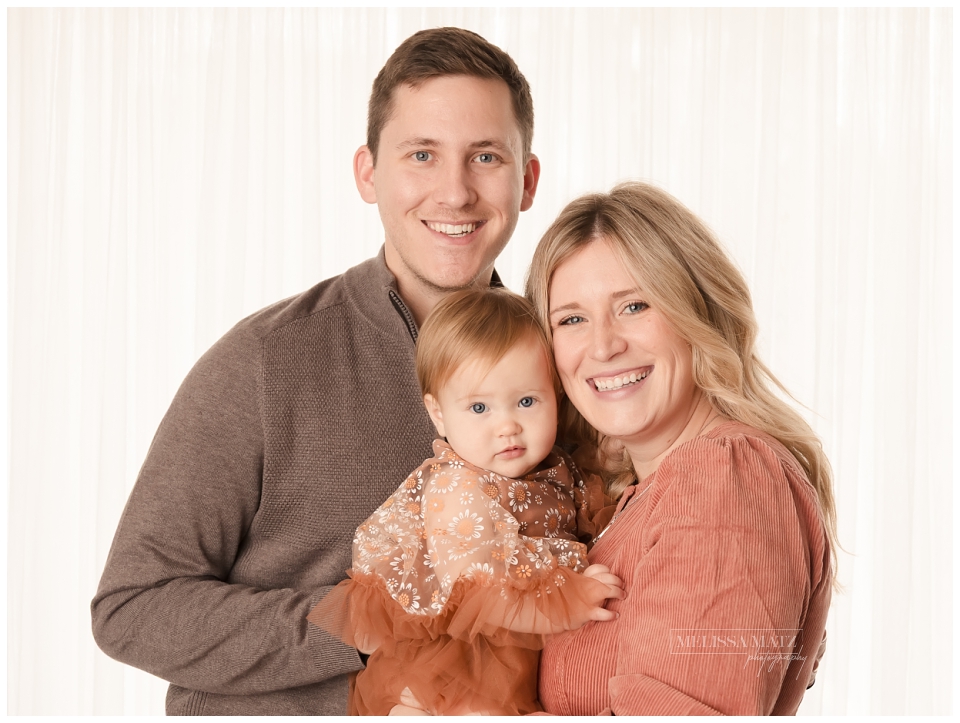 family photo dressed in warm tones in front of a window at their one year milestone studio session