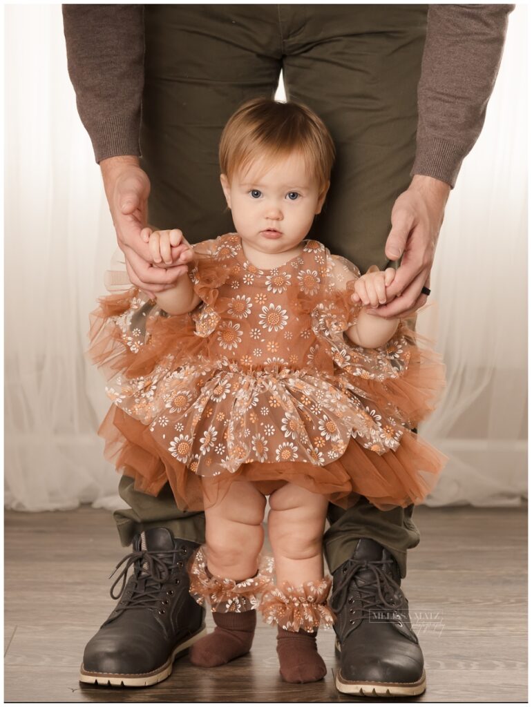 little one year old standing with the help of her dad during her one year photo session