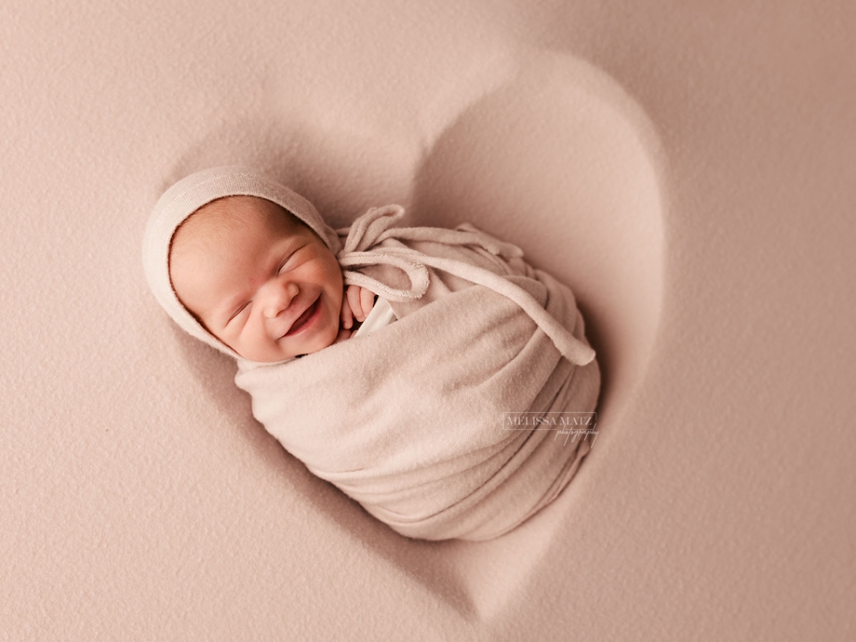 smiling tiny newborn baby swaddle wrapped in a heart prop