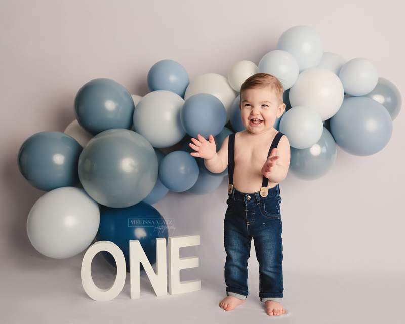 one year cake smash photo session with white and blue balloon garland