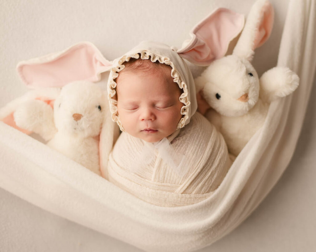 swaddle wrapped newborn with bunny bonnet and bunny plushies