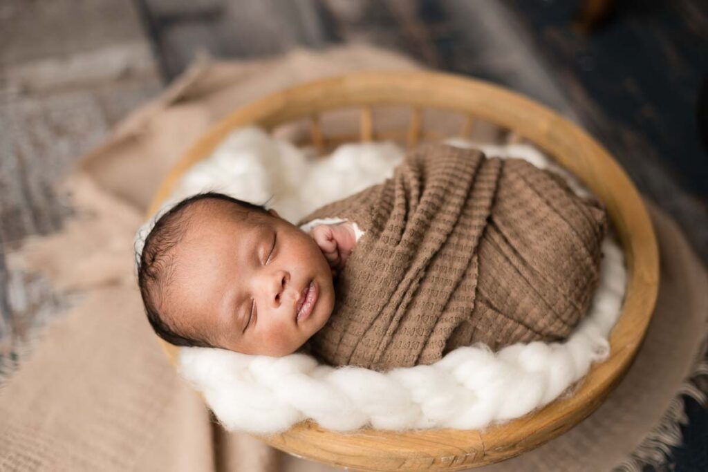 swaddle wrapped newborn in round basket at his metro detroit newborn session