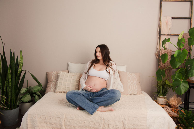 Mom in jeans and a simple tank holding her belly in a light and airy photography studio