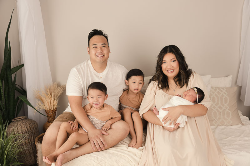 Family with newborn and older siblings in coordinated neutral outfits during a studio newborn session