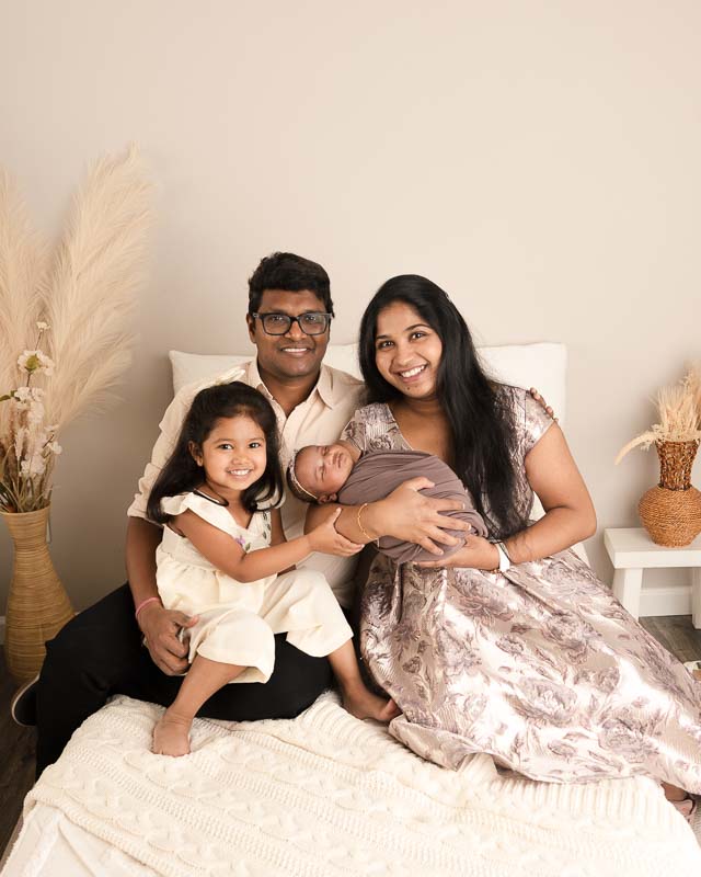 Family of four in coordinated outfits of soft purples and cream during a newborn photography session in a light and airy studio