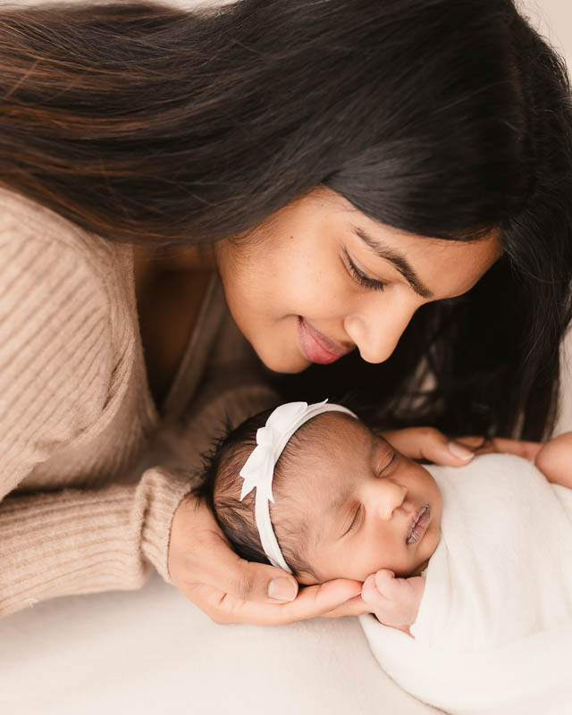 New mother gazing down at her newborn baby during a professional newborn photography session in Metro Detroit