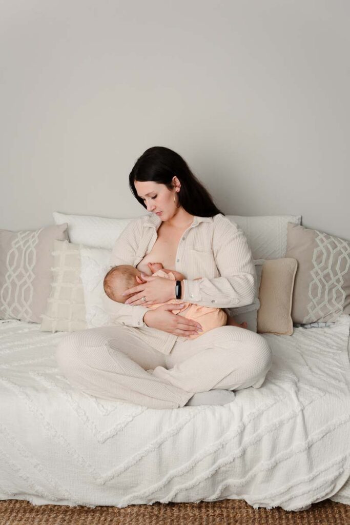 soft creams and airy studio photo of nursing mom looking down at her newborn baby cradled in her arms