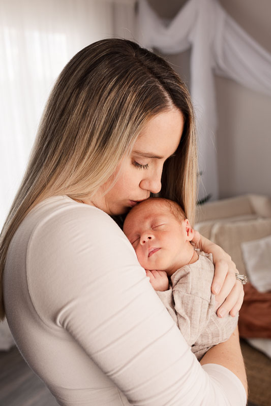 Mother cradling newborn face-to-face, quiet connection captured in soft studio light
