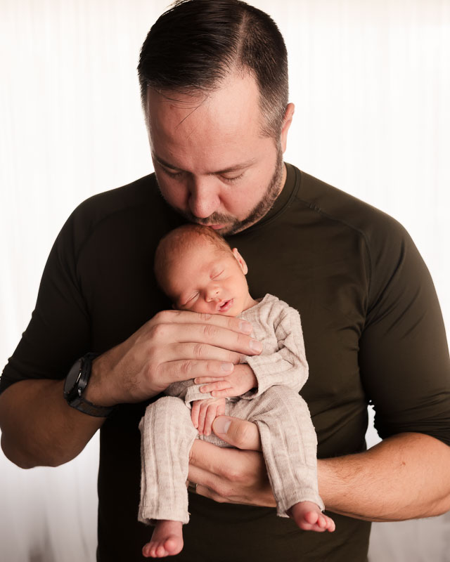 Father holding newborn upright against his chest, strong and gentle studio portrait