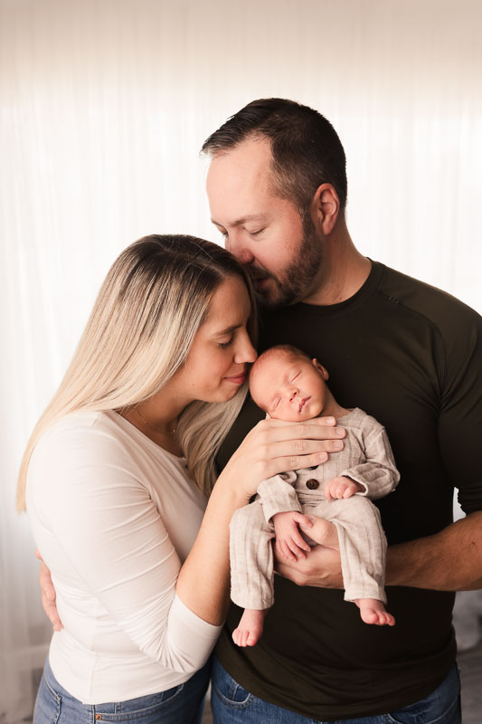 Mother and father facing each other above their newborn, sharing a quiet connected moment