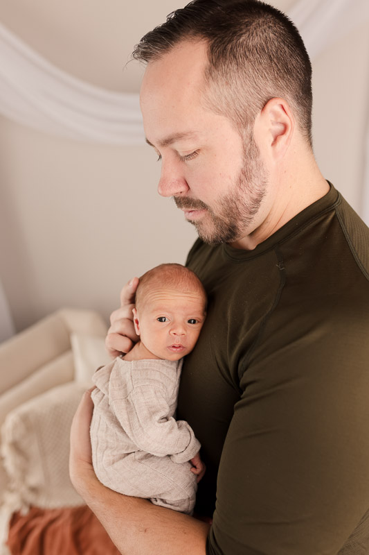 Father holding awake newborn baby on his chest studio lifestyle newborn session