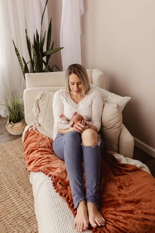 Parent cradling newborn on lap in a bright, airy studio corner