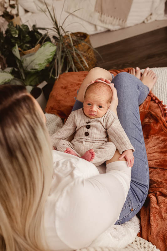 mom holding awake newborn in a studio chair with warm natural light in metro detroit photo studio