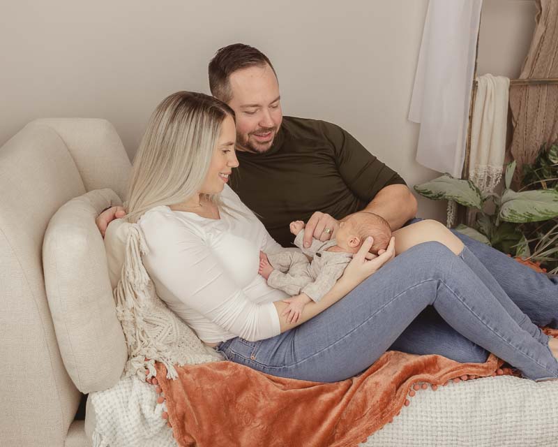Parent relaxed on studio couch, newborn resting peacefully on moms lap