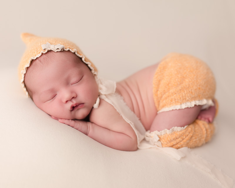 Sleeping newborn curled up with tiny hands cupping her cheek during Shelby Township newborn session