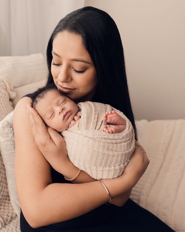 Tired new mother cradling her sleeping newborn baby during the first two weeks of motherhood, captured by a Metro Detroit newborn photographer