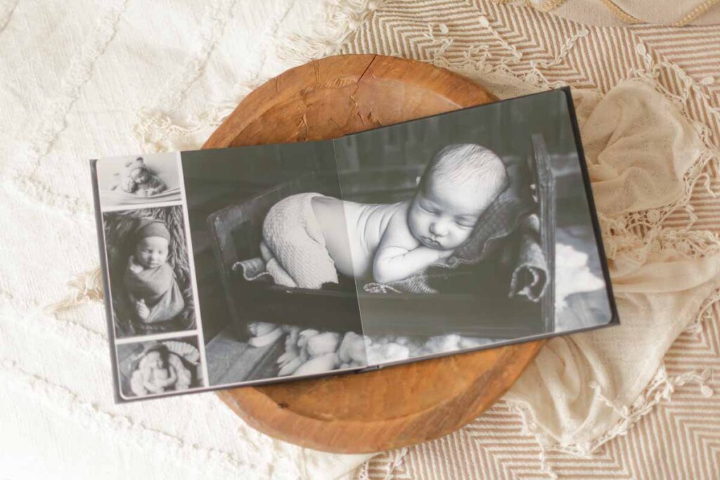 Open flush mount newborn photo album displaying black and white newborn images on a wooden tray