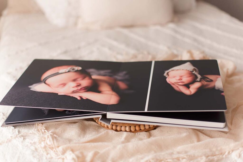 Open flush mount newborn photo album showing newborn detail images on a bed with beaded wooden tray