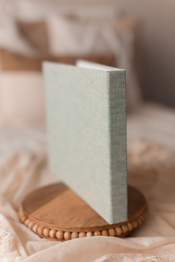 Newborn photo album with sage linen cover standing upright on a wooden tray at Melissa Matz Photography