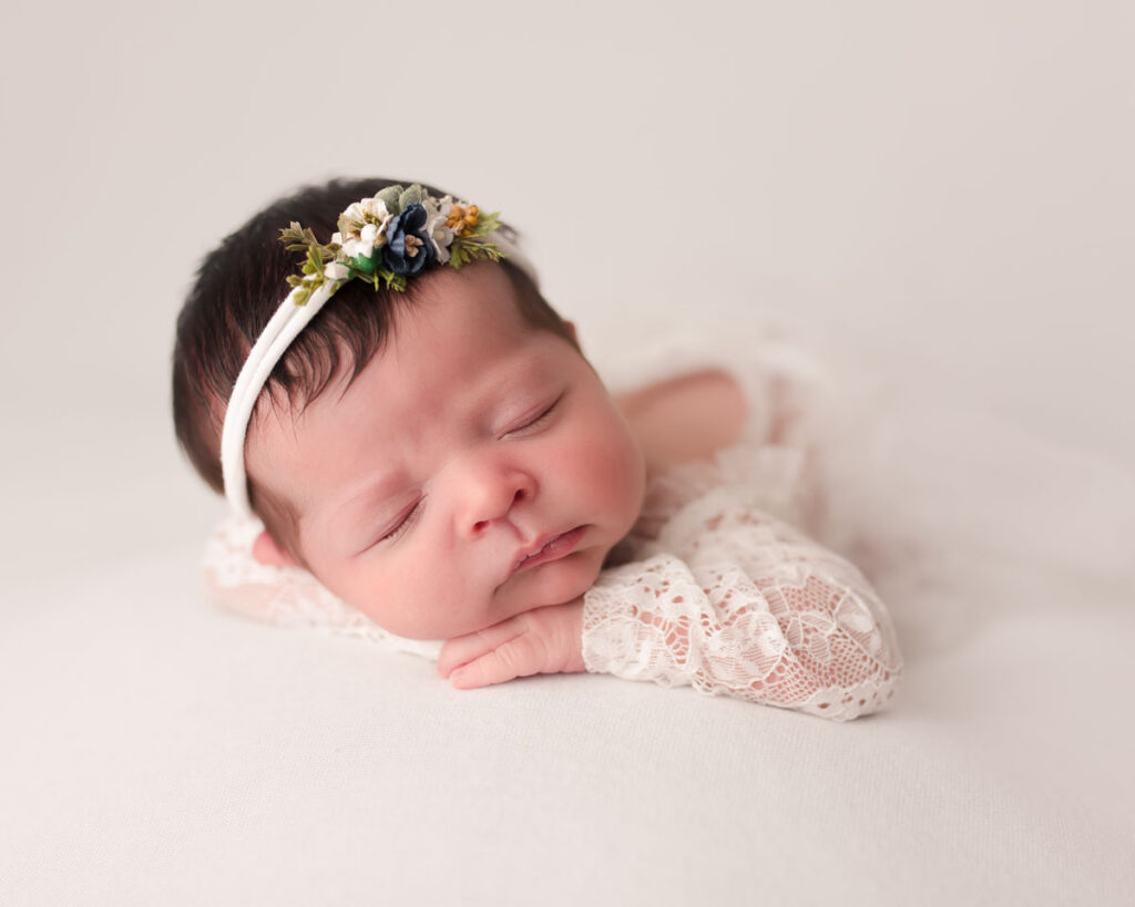 Sleeping newborn baby girl in white lace romper and floral headband during a studio newborn session at Melissa Matz Photography in Shelby Township