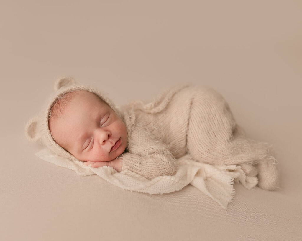 Sleeping newborn baby in cream knit bear bonnet and outfit during a fine art studio newborn session at Melissa Matz Photography in Shelby Township Michigan