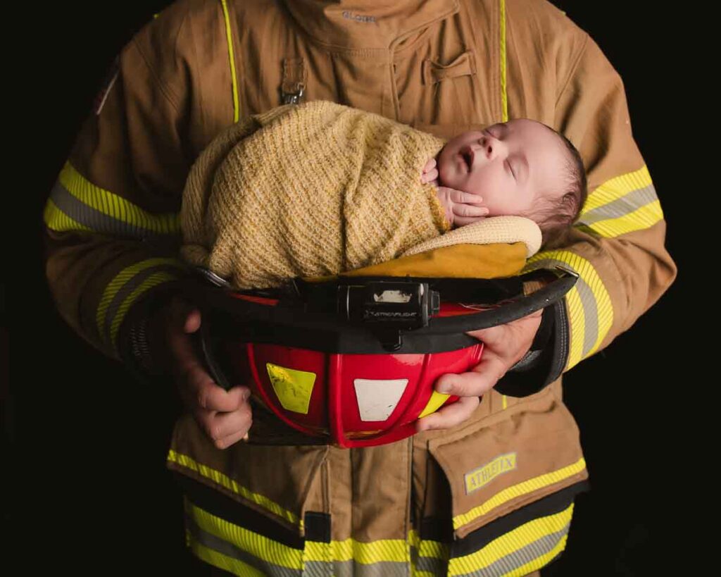 newborn baby held by firefighter parent during posed newborn session Shelby Township Michigan